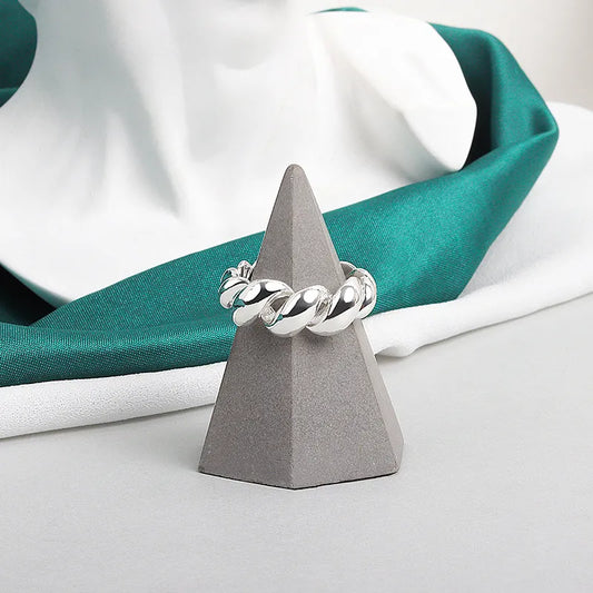 Silberner Ring auf grauem Kegel, Schmuck, glänzend, modernes Design, vor grünem Stoff.