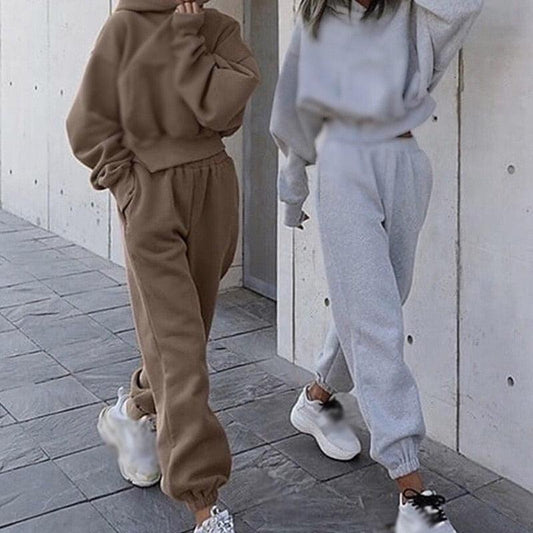 Zwei Frauen in bequemen Jogginganzügen, braun und grau, mit Kapuzenpullover und Jogginghose.