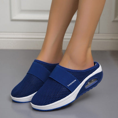 Dunkelblaue Netz-Slipper mit Luftkissen-Sohle, an den Füßen einer Frau vor heller Wand 5