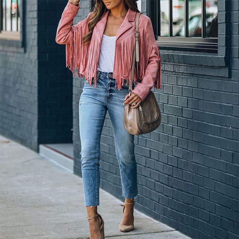 Frau in rosa Fransenjacke, blauer Jeans und beigen High Heels, trägt braune Umhängetasche.