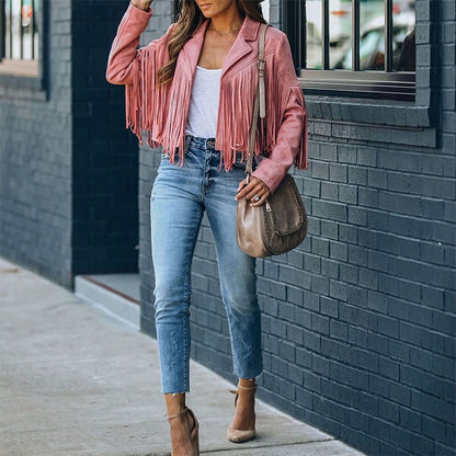 Frau in rosa Fransenjacke, blauer Jeans und beigen High Heels, trägt braune Umhängetasche.
