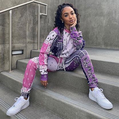 Frau in lila-pinkem Bandana-Print-Trainingsanzug, weiße Sneaker, sitzt auf Treppe.