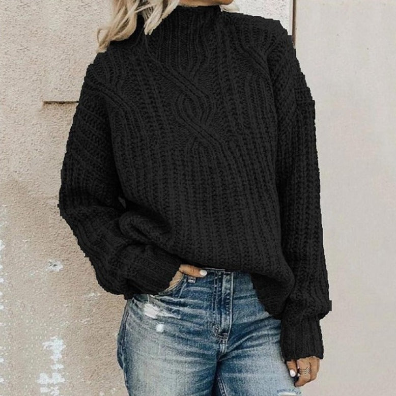 Frau in schwarzem Strickpullover und Jeans vor beiger Wand.