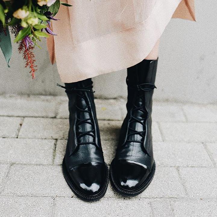 Schwarze Damenstiefel aus Leder, geschnürt, modisch, elegant, auf Pflastersteinen.