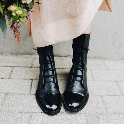 Schwarze Damenstiefel aus Leder, geschnürt, modisch, elegant, auf Pflastersteinen.