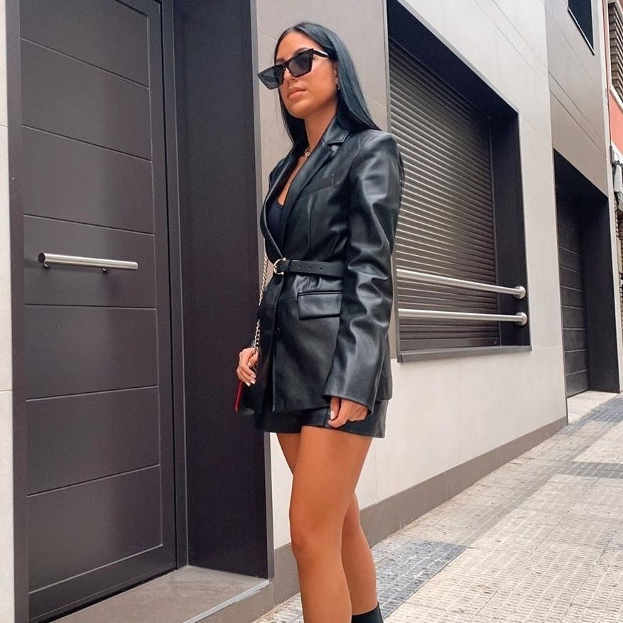 Frau in schwarzem Lederblazer und Sonnenbrille auf städtischer Straße.