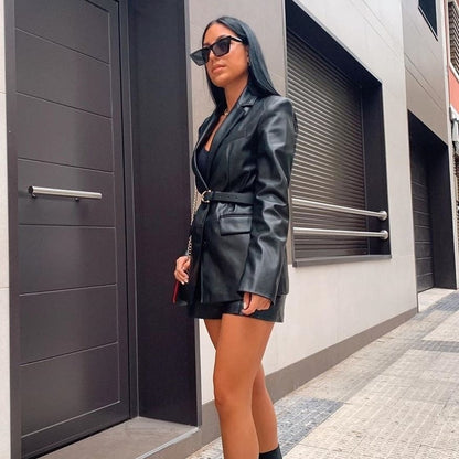 Frau in schwarzem Lederblazer und Sonnenbrille auf städtischer Straße.