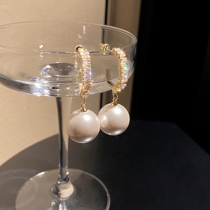 Goldene Ohrringe mit Perlenanhänger, funkelnde Kristalle, eleganter Schmuck, luxuriöses Design.