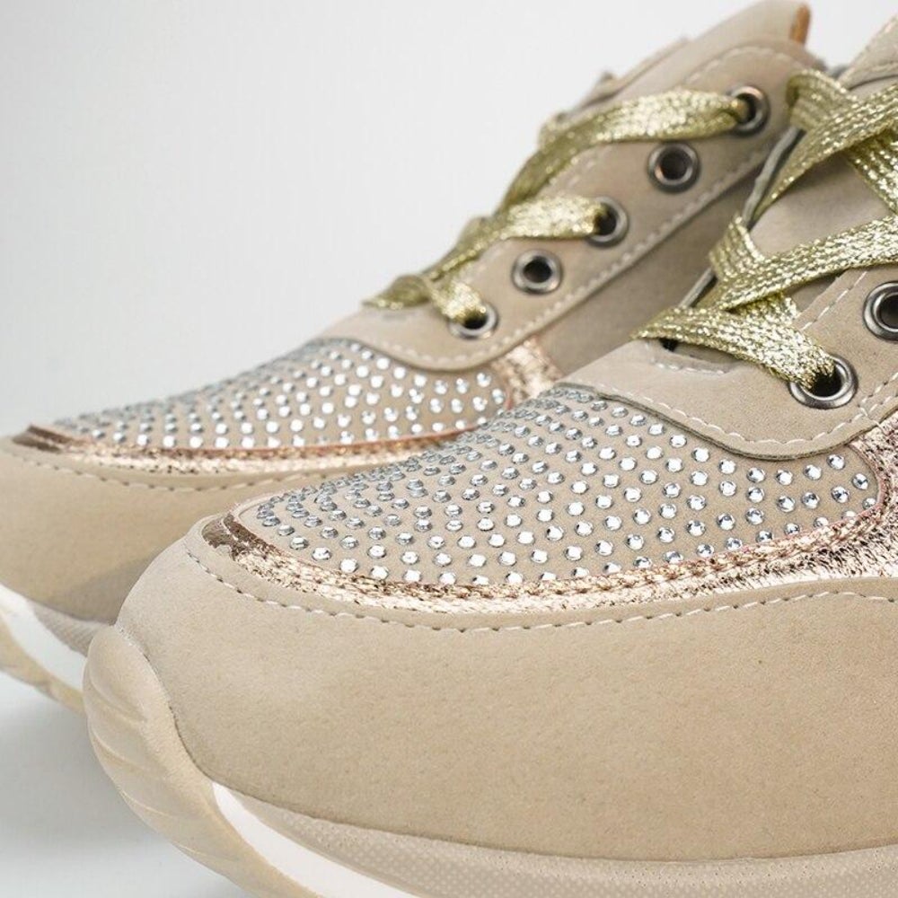 Nahaufnahme der Schuhspitzen mit dicht gesetzten Strasssteinen, goldfarbenen Schnürsenkeln und weicher Sohle am beigen Modell. 10