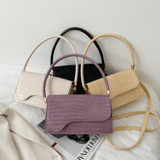 Vier elegante Krokodilleder-Handtaschen in Lila, Schwarz, Beige und Creme auf weißem Hintergrund.