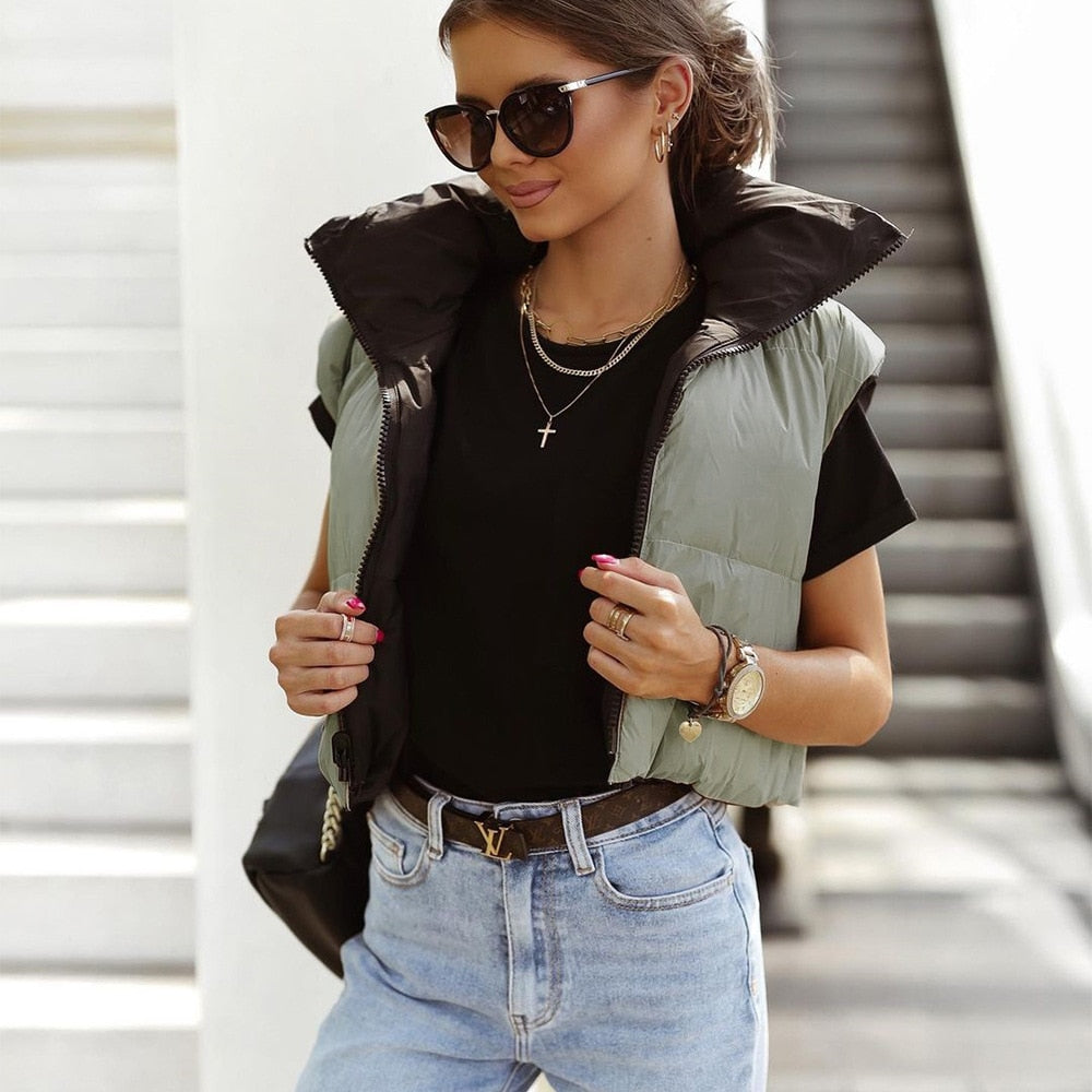 Dame in grüner Steppweste, schwarzem T-Shirt, Sonnenbrille, Jeans, modisch, urbaner Stil.