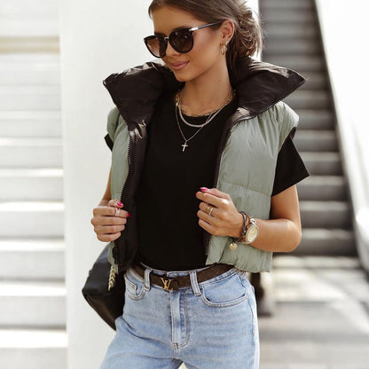 Dame in grüner Steppweste, schwarzem T-Shirt, Sonnenbrille, Jeans, modisch, urbaner Stil.