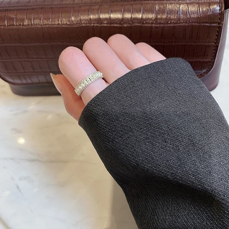 Hand mit funkelndem Diamantring vor brauner Lederhandtasche auf Marmortisch.