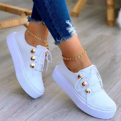 Weiße Damen-Sneaker mit goldenen Knöpfen, Jeans, Holzfußboden, modische Freizeitschuhe.