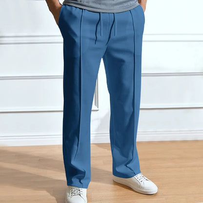 Frontansicht der Hose in Blau, getragen mit grauem Shirt und weißen Sneakern, Kordelzug, Bundfalten und gerader Beinschnitt erkennbar. 5