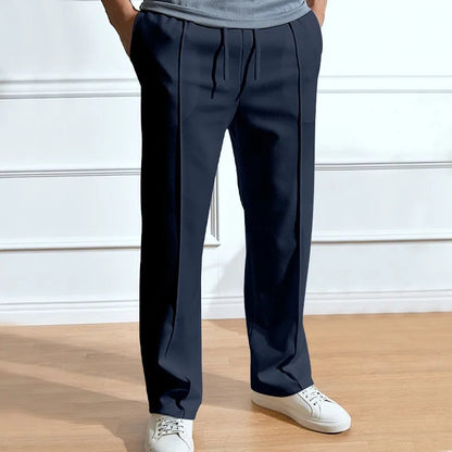 Frontansicht der Hose in Marineblau, getragen mit grauem Shirt und weißen Sneakern, Hände in den Taschen, Bundfalten und Kordelzug sichtbar. 1