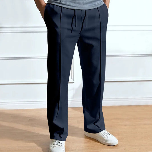 Frontansicht der Hose in Marineblau, getragen mit grauem Shirt und weißen Sneakern, Hände in den Taschen, Bundfalten und Kordelzug sichtbar. 1