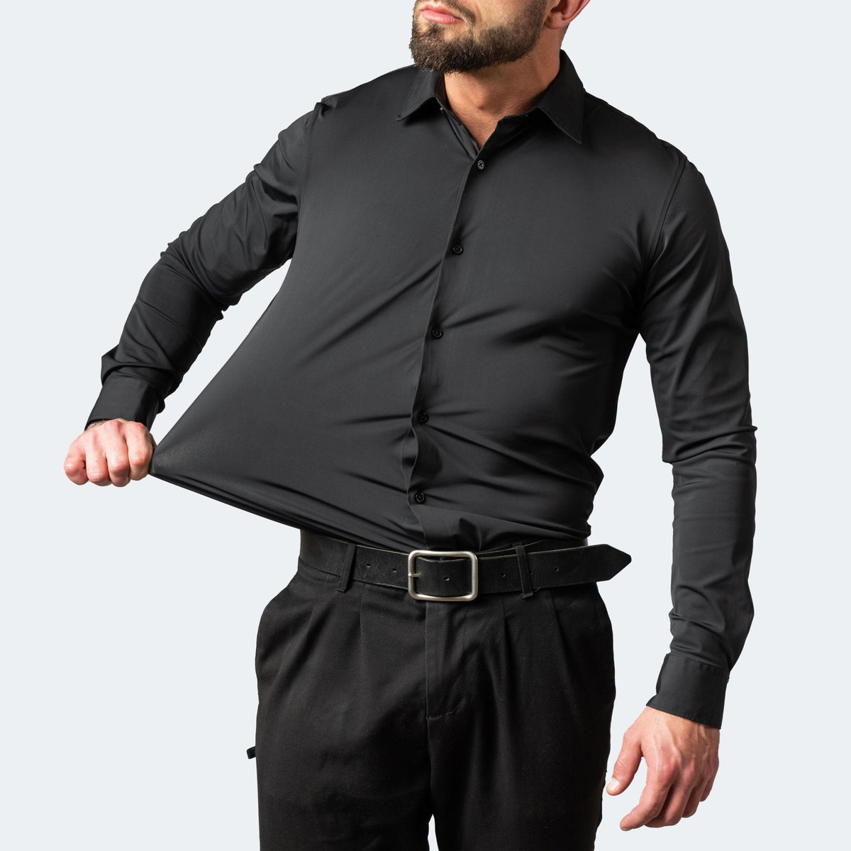 Mann im schwarzen Hemd zieht den Stoff seitlich am Bauch weit auseinander, dazu schwarze Hose und Gürtel 4