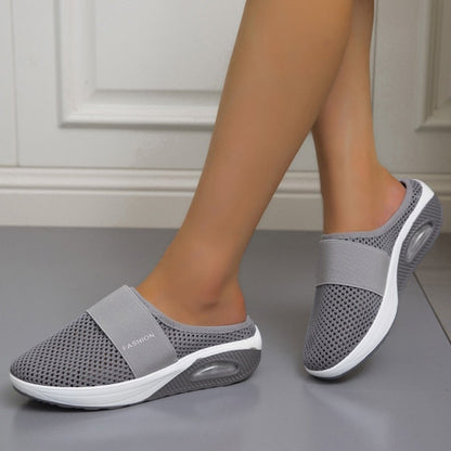 Graue Netz-Slipper mit Luftkissen-Sohle, von einer Frau auf grauem Boden getragen 2