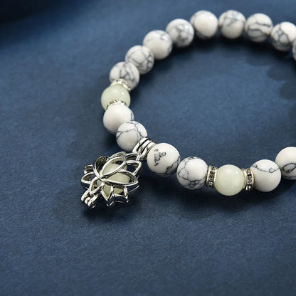 Armband aus weißen Marmorperlen mit silbernem Lotus-Anhänger auf blauem Hintergrund.