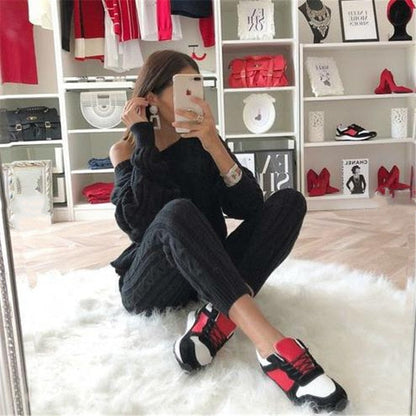 Frau in schwarzem Outfit mit rot-weißen Sneakers, sitzt auf weißem Teppich, modische Kleidung.