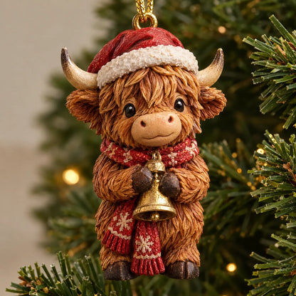 Nahaufnahme einer Hochlandkuh-Figur mit Weihnachtsmütze, rotem Schneeflockenschal und goldener Glocke, an einem Tannenzweig hängend. 3