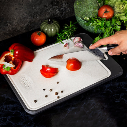 Küchenmesser schneidet Tomaten auf Schneidebrett, umgeben von Paprika und Gemüse.
