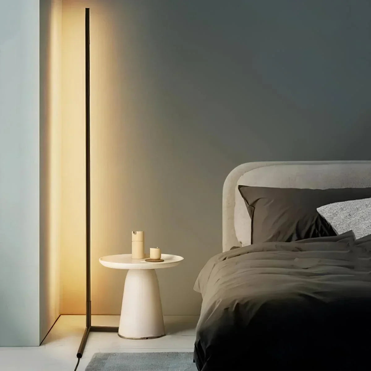 Schmale Stehleuchte strahlt warmes Licht an die Wand, daneben ein cremefarbener Beistelltisch und ein Bett 1