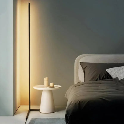 Schmale Stehleuchte strahlt warmes Licht an die Wand, daneben ein cremefarbener Beistelltisch und ein Bett 1