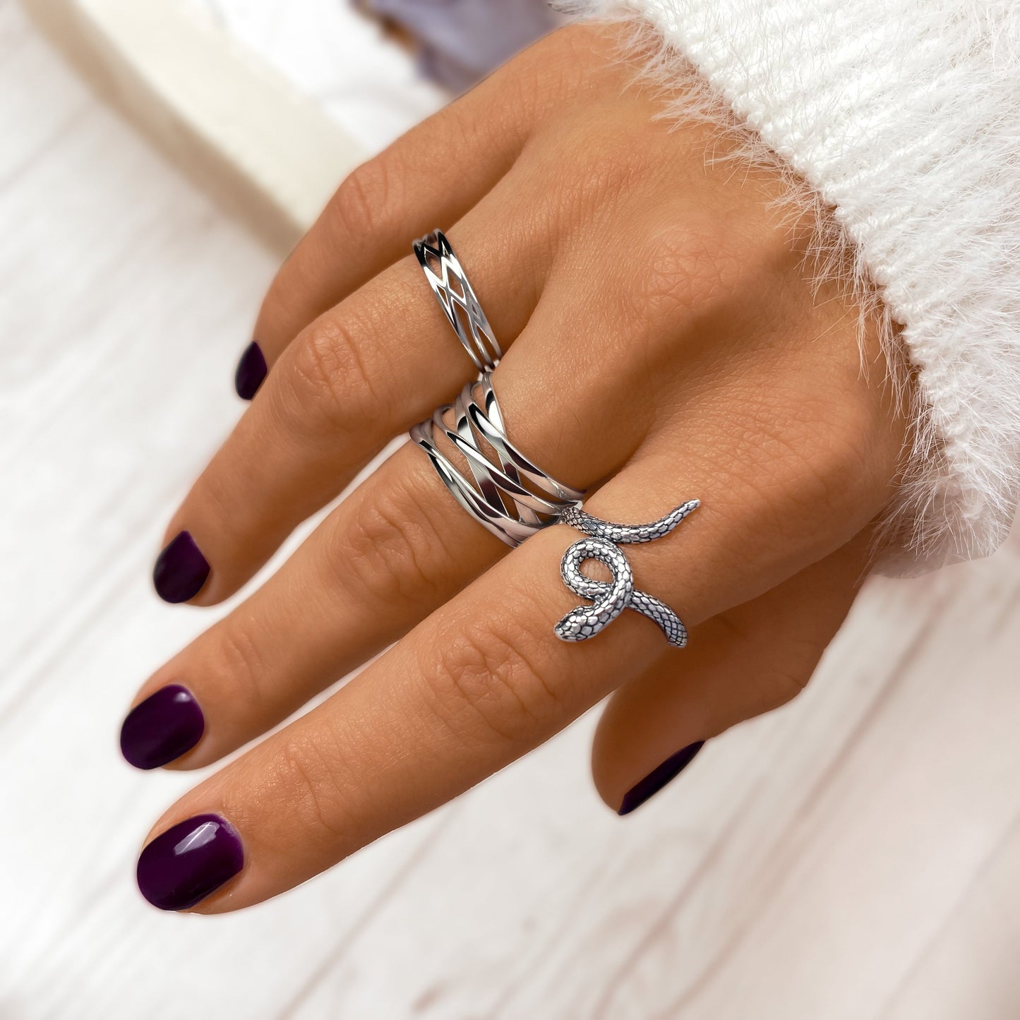 Hand mit silbernen Ringen, lila Nagellack, elegantes Schmuckdesign, Nahaufnahme.