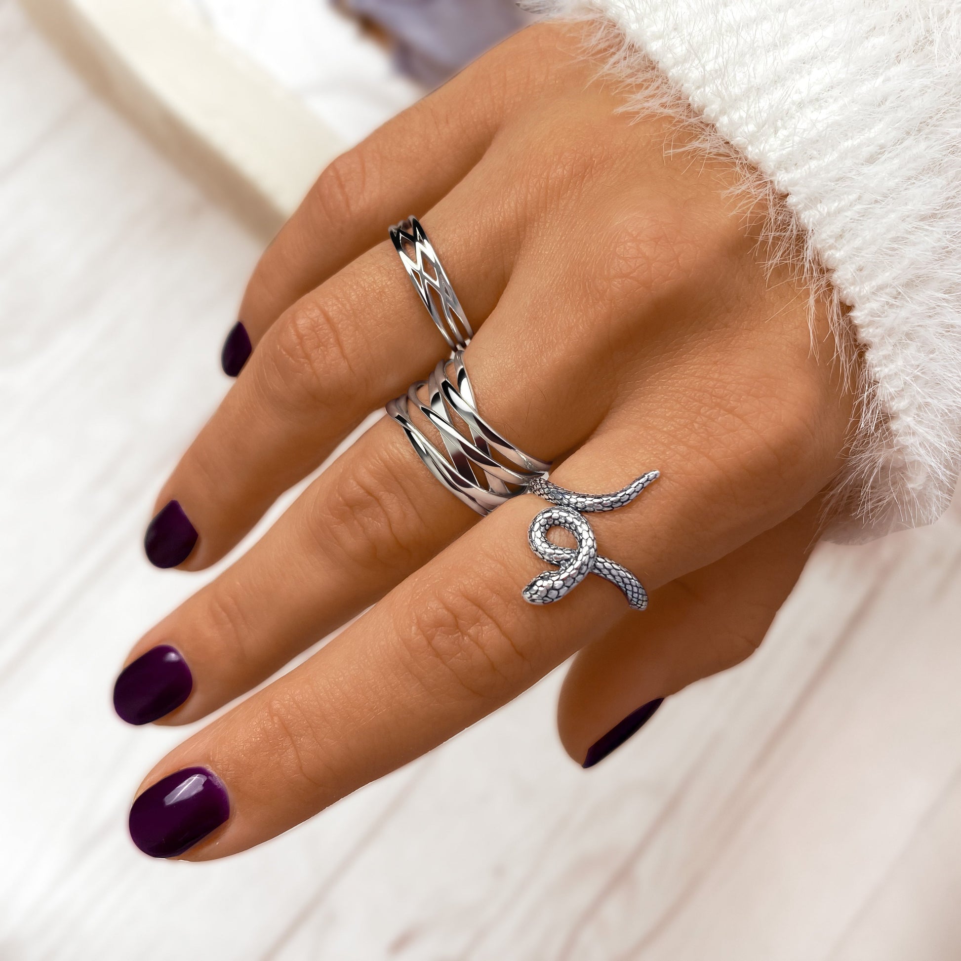 Hand mit silbernen Ringen, lila Nagellack, elegantes Schmuckdesign, Nahaufnahme.