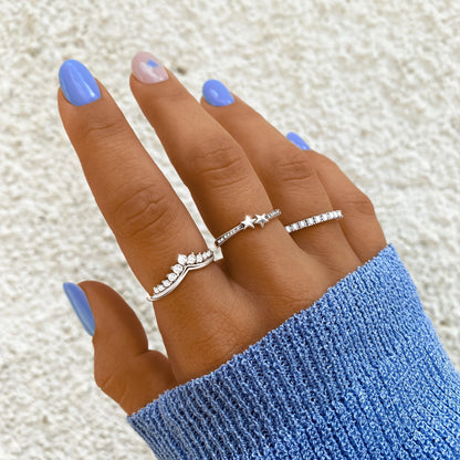 Frau mit blauen Nägeln trägt drei silberne Ringe, einer mit Stern, auf blauer Strickjacke.