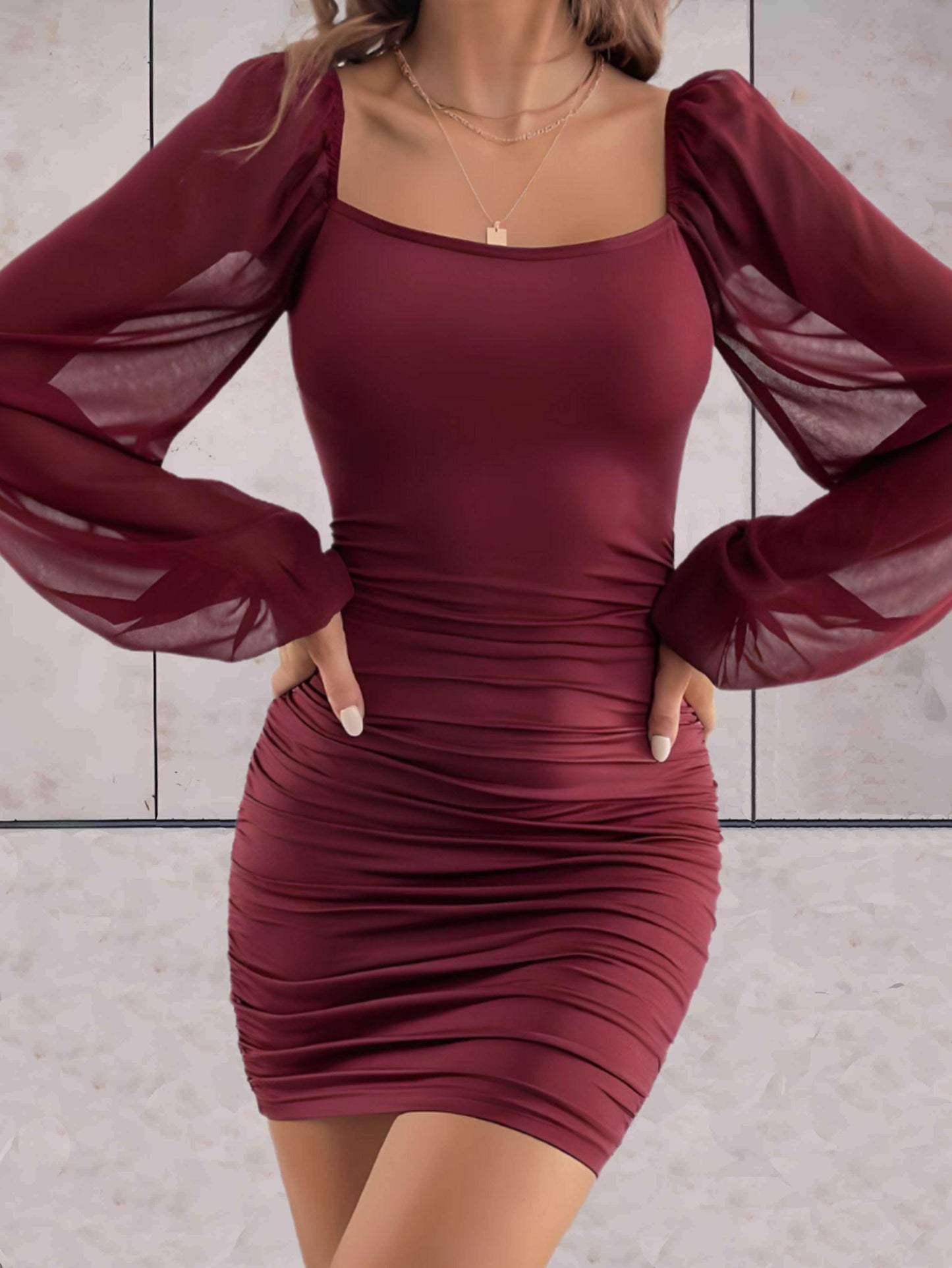 Frau in bordeauxfarbenem, figurbetontem Kleid mit langen, transparenten Ärmeln.