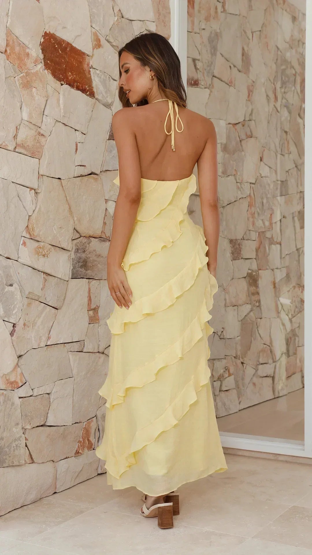 Rückansicht: Das gelbe Maxikleid mit rückenfreiem Neckholder-Band und diagonal verlaufenden Rüschen am Rock 2