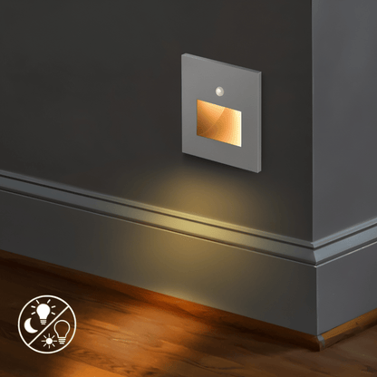 Graue Wandleuchte mit Sensor und warm leuchtender Öffnung wirft Licht auf Sockelleiste und Holzboden 5