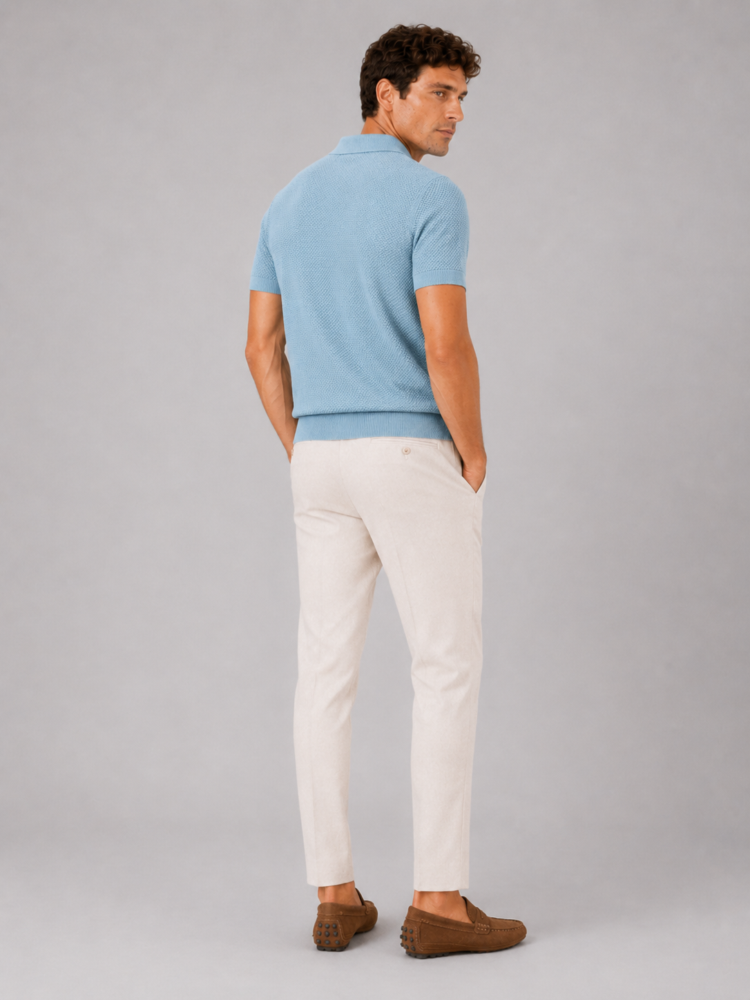 Rückansicht des hellblauen Poloshirts am Model, kurze Ärmel und Rippbündchen am Saum, dazu helle Hose und braune Mokassins 4