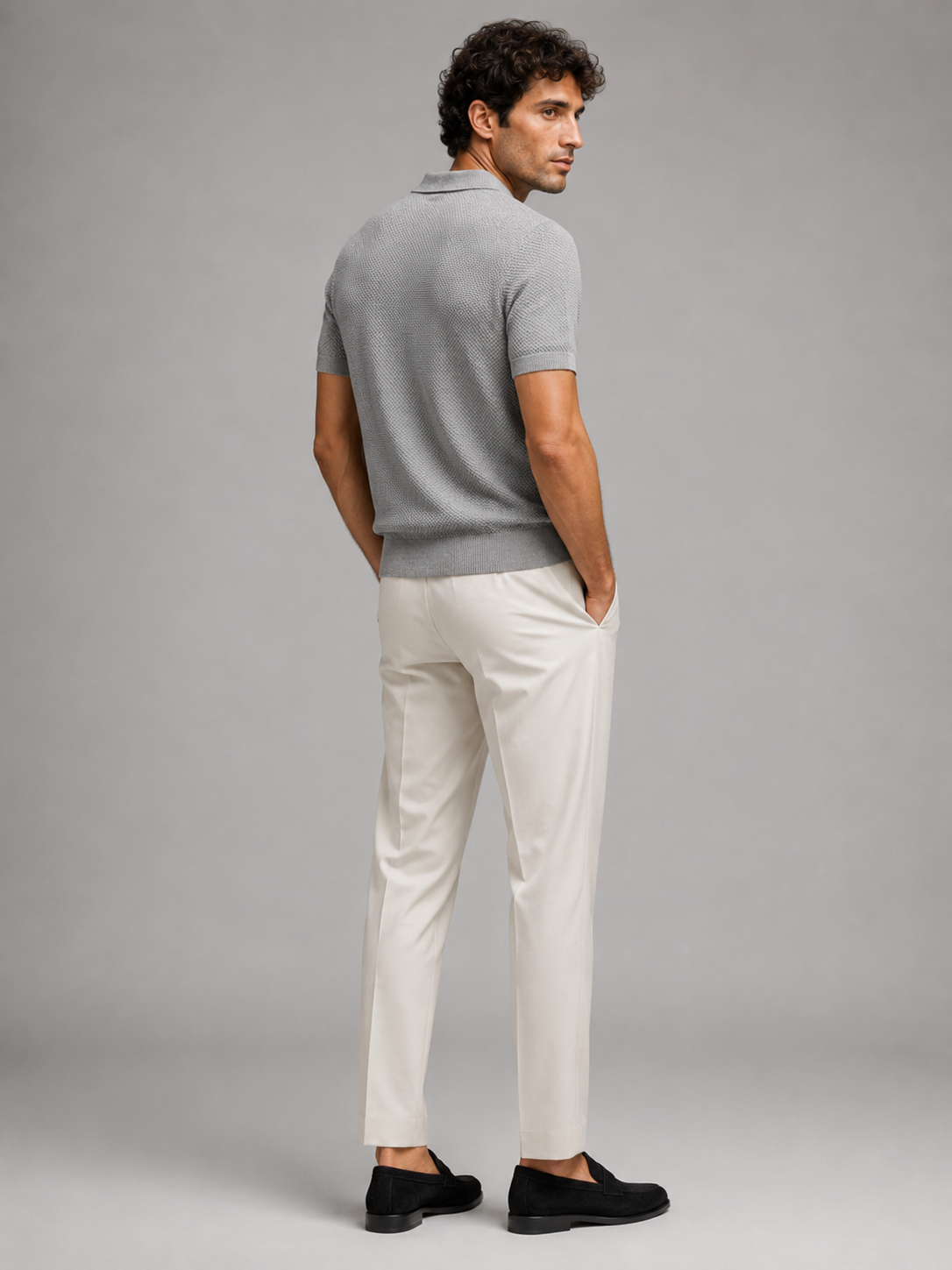 Rückansicht des grauen Strickpolos mit Strukturmuster, Model blickt zur Seite, cremeweiße Hose 29