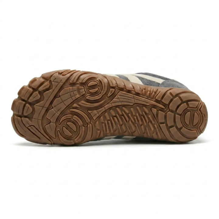 Sohlenansicht des grauen Schuhs mit braunem Gummiprofil, Zehenstollen und rundem Fersenmuster, beige Streifen am Rand sichtbar. 9