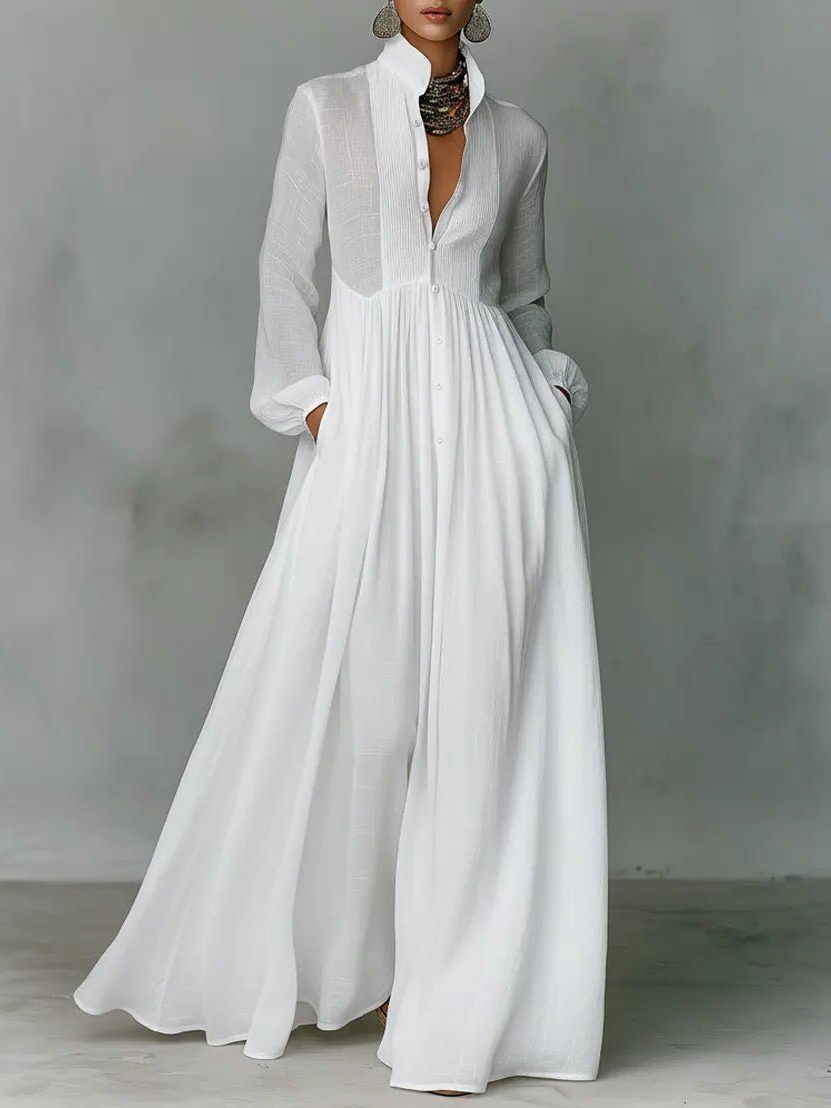 Weißes Maxikleid mit Stehkragen und Knopfleiste, getragen von einem Model mit Statement-Kette, Hände in den Taschen 1