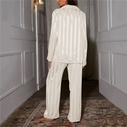 Frau in cremefarbenem Satin-Pyjama, gestreift, steht in elegantem Flur.