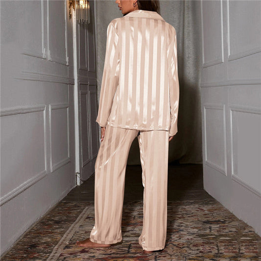 Frau in cremefarbenem Satin-Pyjama, gestreift, steht in elegantem Flur.