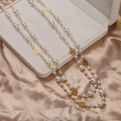 Lange Perlenkette mit goldenen Rosenanhängern auf beigem Stoff in Schmuckschatulle.