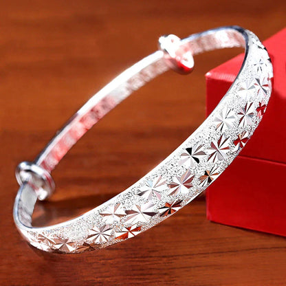 Silberarmreif mit Sternmuster, glänzend, Damen-Schmuck, Geschenk, auf Holztisch.