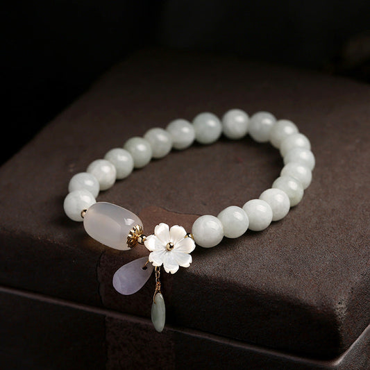 Jade-Armband mit Blumenanhänger, weißer Perle und goldenen Akzenten auf dunklem Hintergrund.