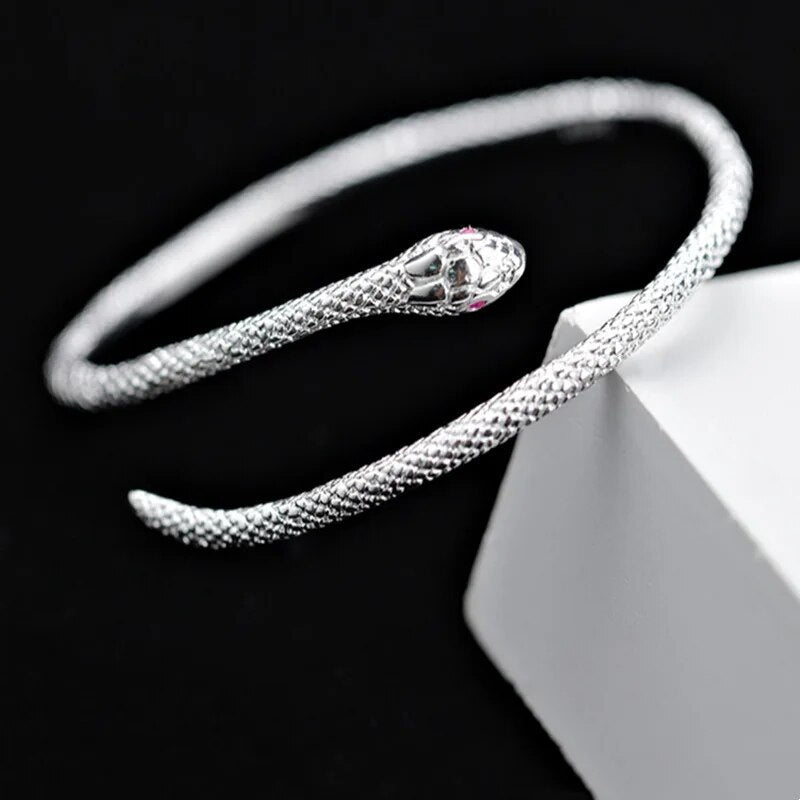Silbernes Schlangenarmband, offenes Design, strukturiert, eleganter Schmuck auf schwarzem Hintergrund.