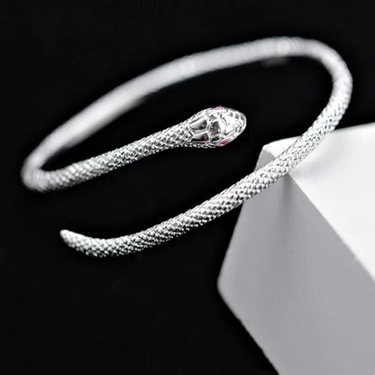 Silbernes Schlangenarmband, offenes Design, strukturiert, eleganter Schmuck auf schwarzem Hintergrund.