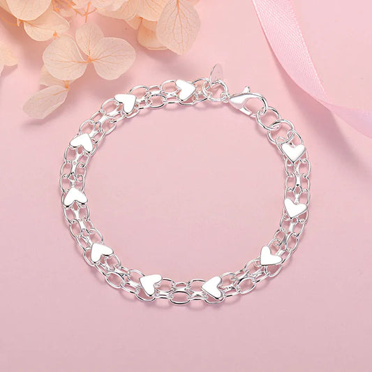 Silberarmband mit Herzanhängern auf rosa Hintergrund, eleganter Schmuck für Damen.