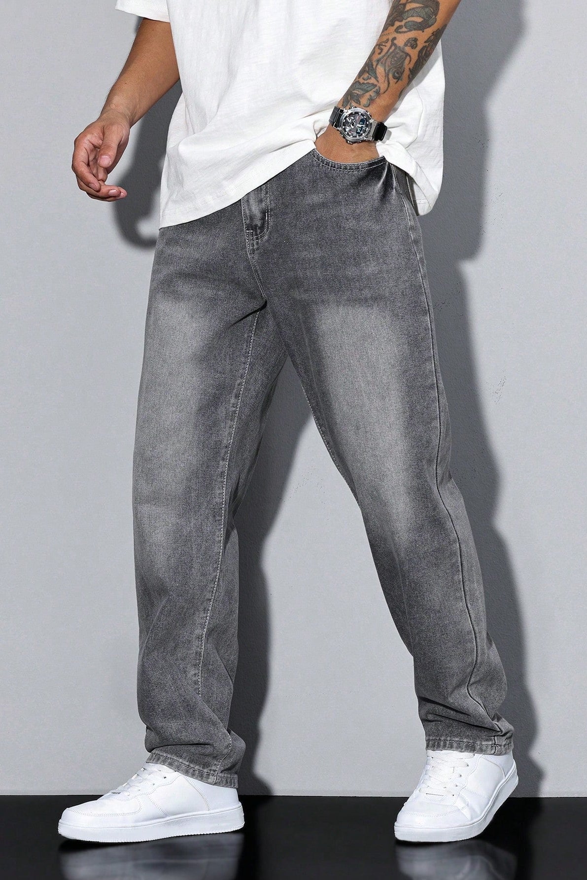 Seitlich fotografierte graue Jeans mit Waschung, getragen zu weißem Shirt, Armbanduhr und weißen Sneakern, Hand in der 5