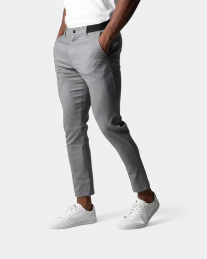 Mann trägt die schmale, knöchellange Hose in Grau mit weißem Shirt und Sneakern, Hände in den Taschen 1