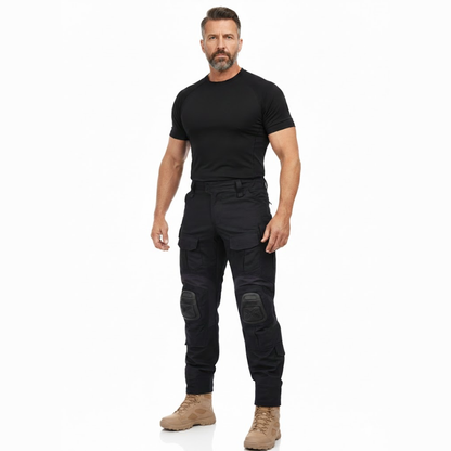 Bärtiger Model-Mann in schwarzem Shirt und schwarzer Hose mit Knieschonern, beigen Stiefeln, Ganzkörperansicht von vorn. 7